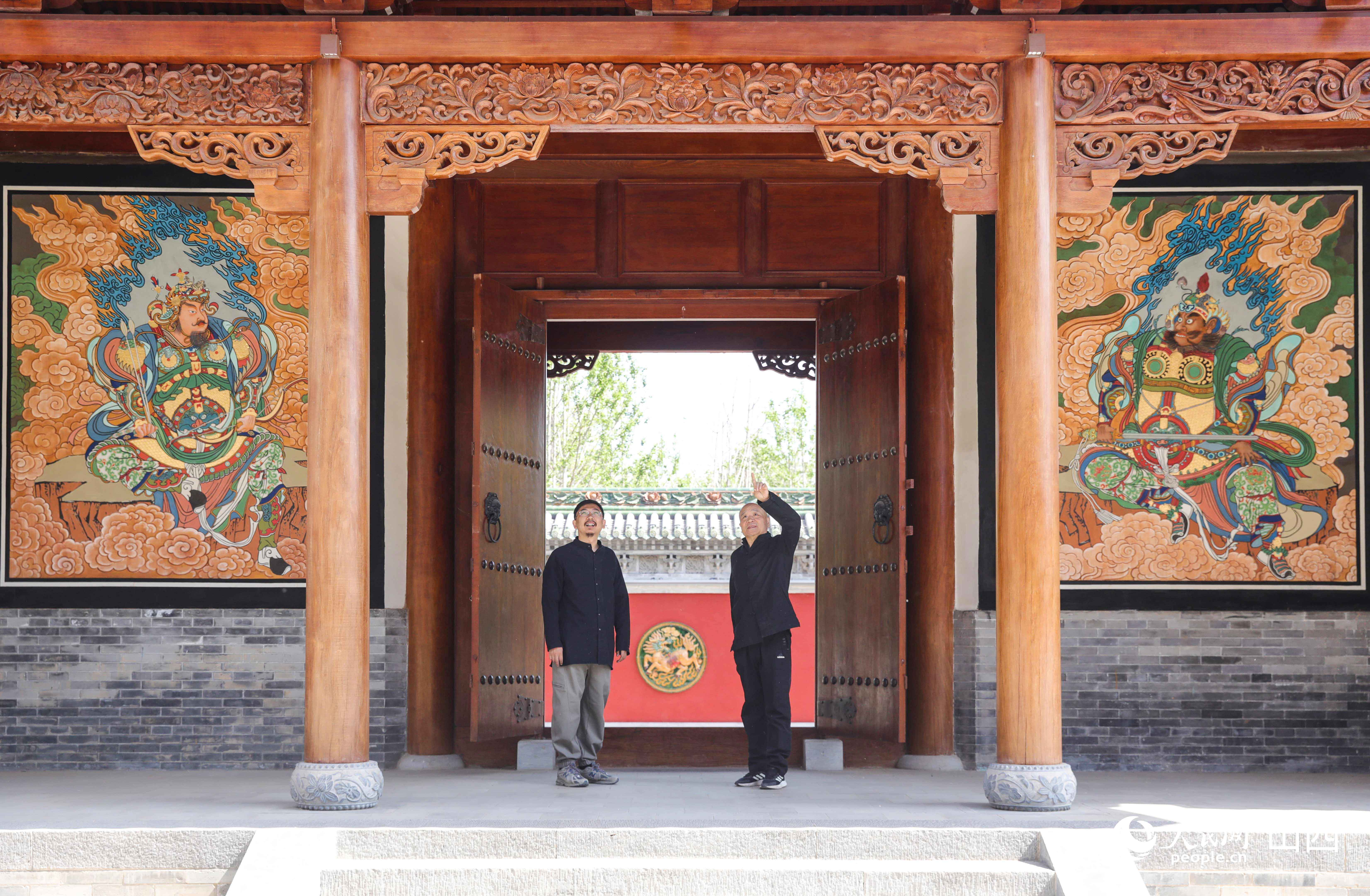 劉惠斌與劉子群站在關帝廟壁畫前交談。